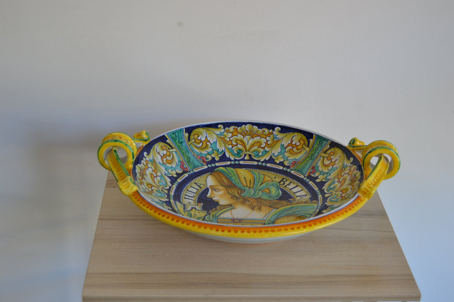 Centrotavola con manici dipinto a mano in ceramica tornito a mano cm 42. Un pezzo classico della tradizione derutese. Al centro figura femminile Rinascimentale e con bordo Delfini