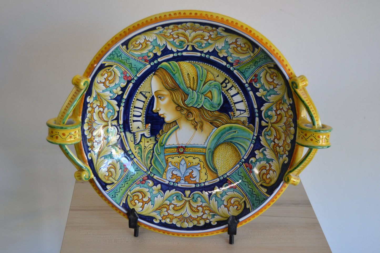 Centrotavola con manici dipinto a mano in ceramica tornito a mano cm 42. Un pezzo classico della tradizione derutese. Al centro figura femminile Rinascimentale e con bordo Delfini